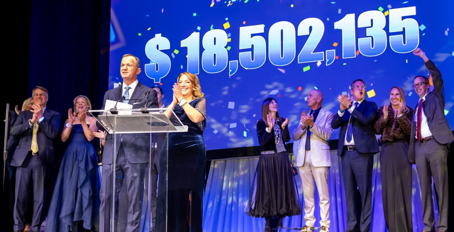 people clapping on a stage in front of a banner reading $18,502