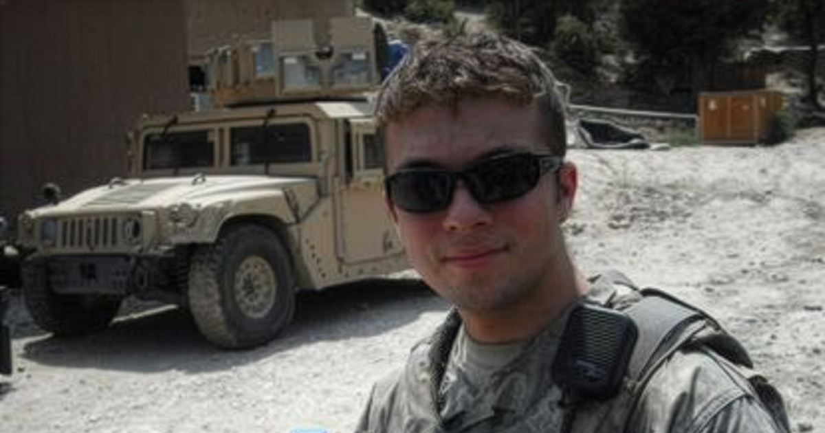 white male with glasses and military uniform standing in front of army truck 