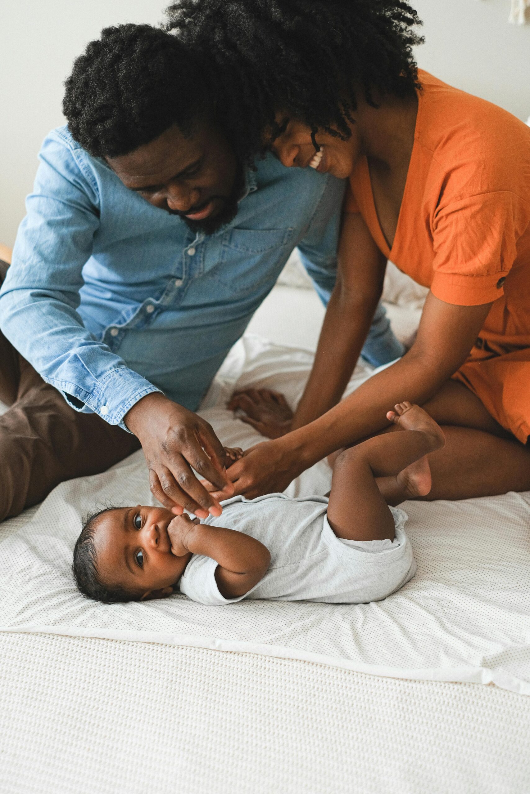 baby laying on his back with two parents sitting over him
